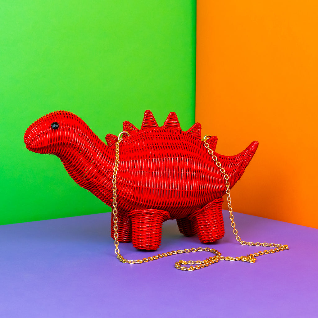 Wicker darling Othniel the steasaurus dinosaur purse is bright red and sits in a colourful background.