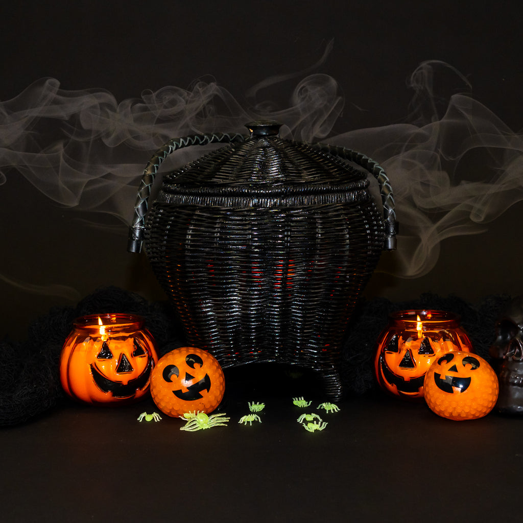 A rattan wicker bag in the shape of a cauldron. Painted black, with a black braided leather handle.
