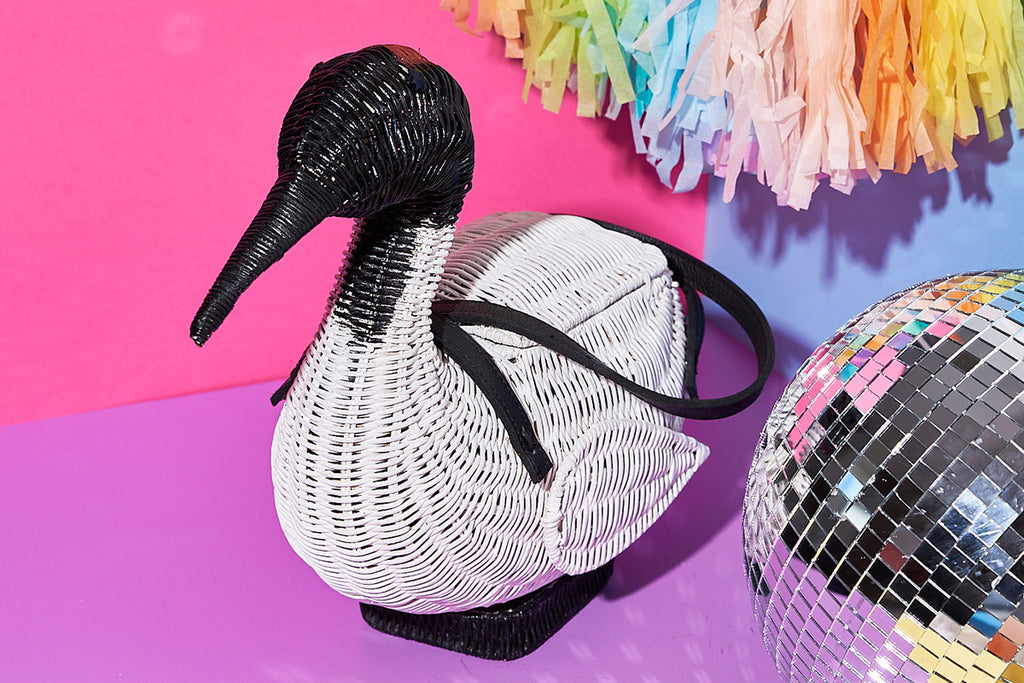 Animal shaped purse A white ibis with black face and tail is the inspiration for this ibis shaped bag by Wicker Darling. The bag sits in front of a paper party wall with a silver disco ball appearing to one side. 