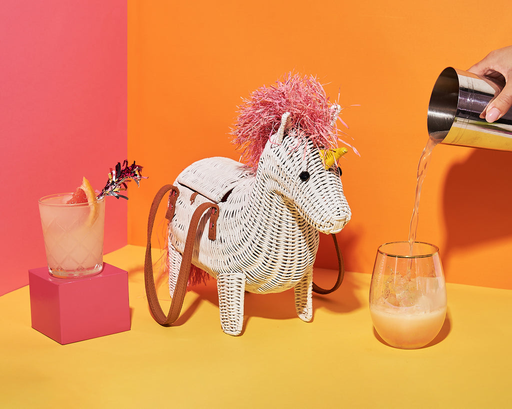 Animal shaped purse unicorn shaped handbag sits with a cocktail in a colourful room
