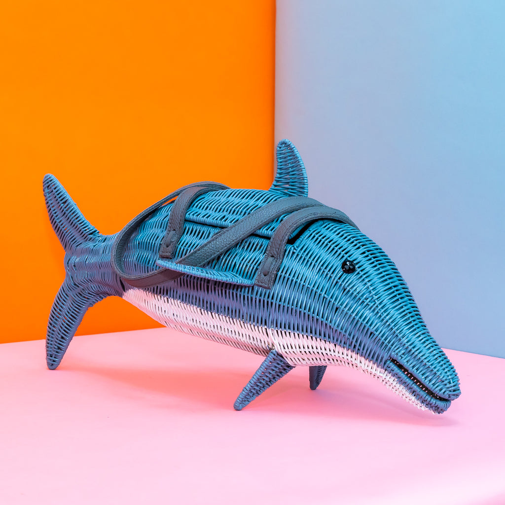 A dolphin-style mystery sea friend wicker purse sits in a colourful background