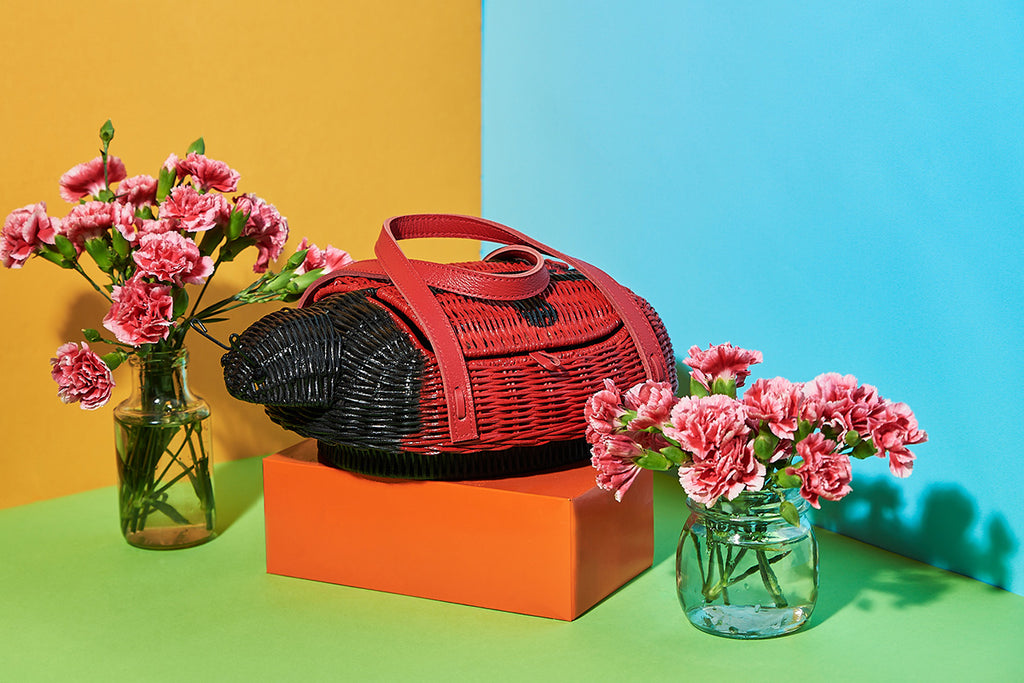Animal shaped purse A ladybug shaped handbag sits amongst flowers in a colourful scene. The Wicker Darling original is black and red and features a high quality leather strap.