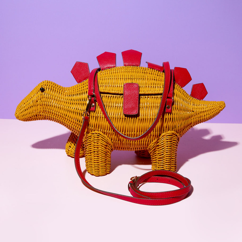 Wicker Darling's stegosaurus bag dinosaur shaped purse is a yellow dinosaur wth red leather detailing in a colourful room 