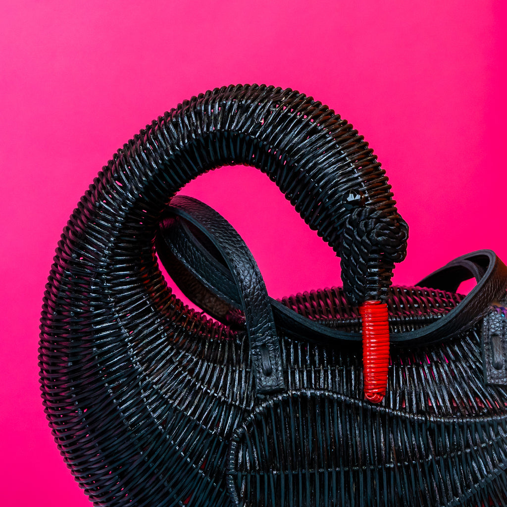 Wicker darling Odile the black swan purse swan handbag sits in a colourful background.