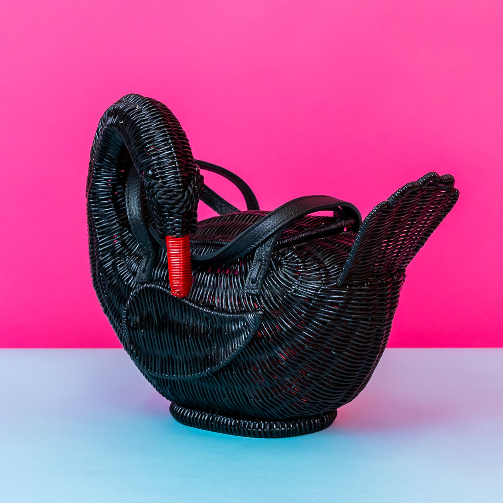 Wicker darling Odile the black swan purse swan handbag sits in a colourful background.