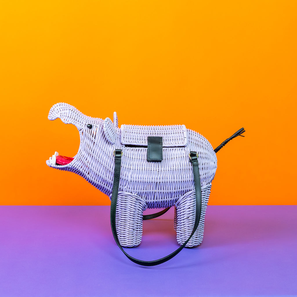 Wicker Darling Hestia the hippo shaped bag sits in a colourful background.