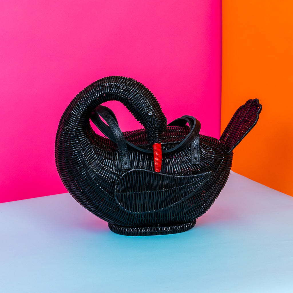 Wicker darling Odile the black swan purse swan handbag sits in a colourful background.