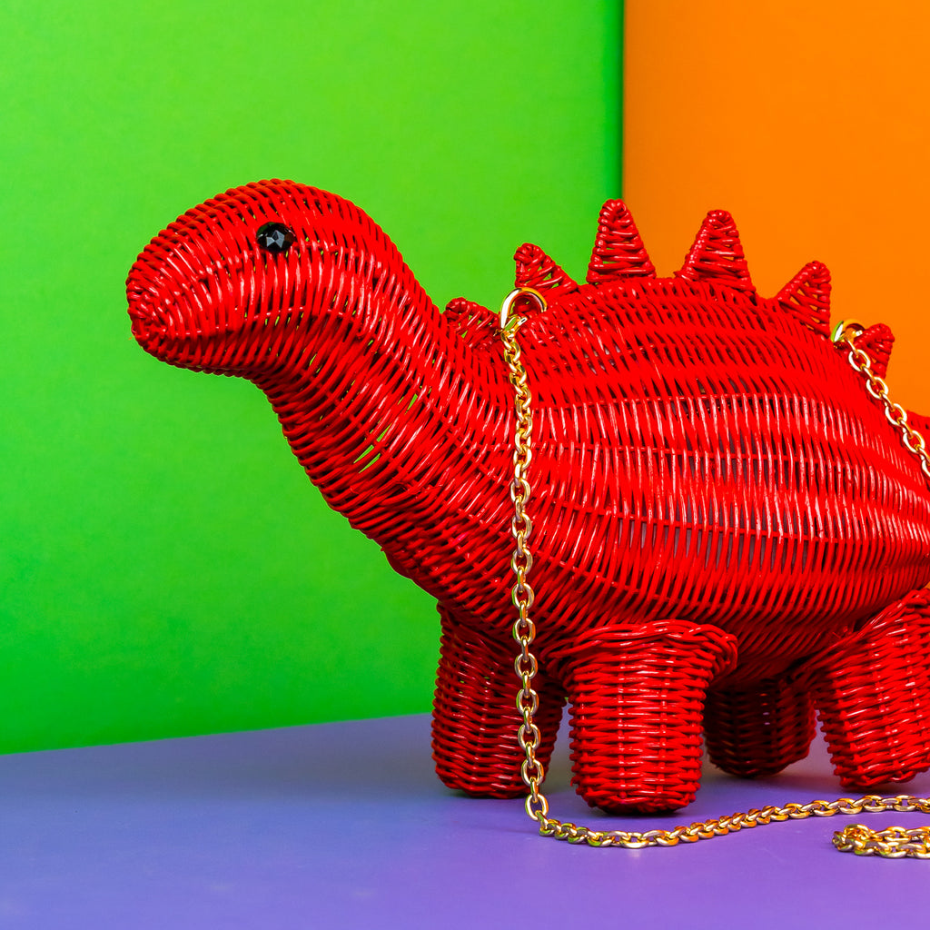 Wicker darling Othniel the steasaurus dinosaur purse is bright red and sits in a colourful background.