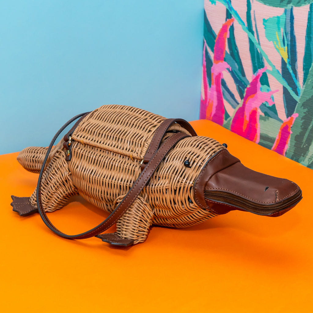 Wicker Darling Platypurse II platypus bag design wicker handbag sits in a colourful background.