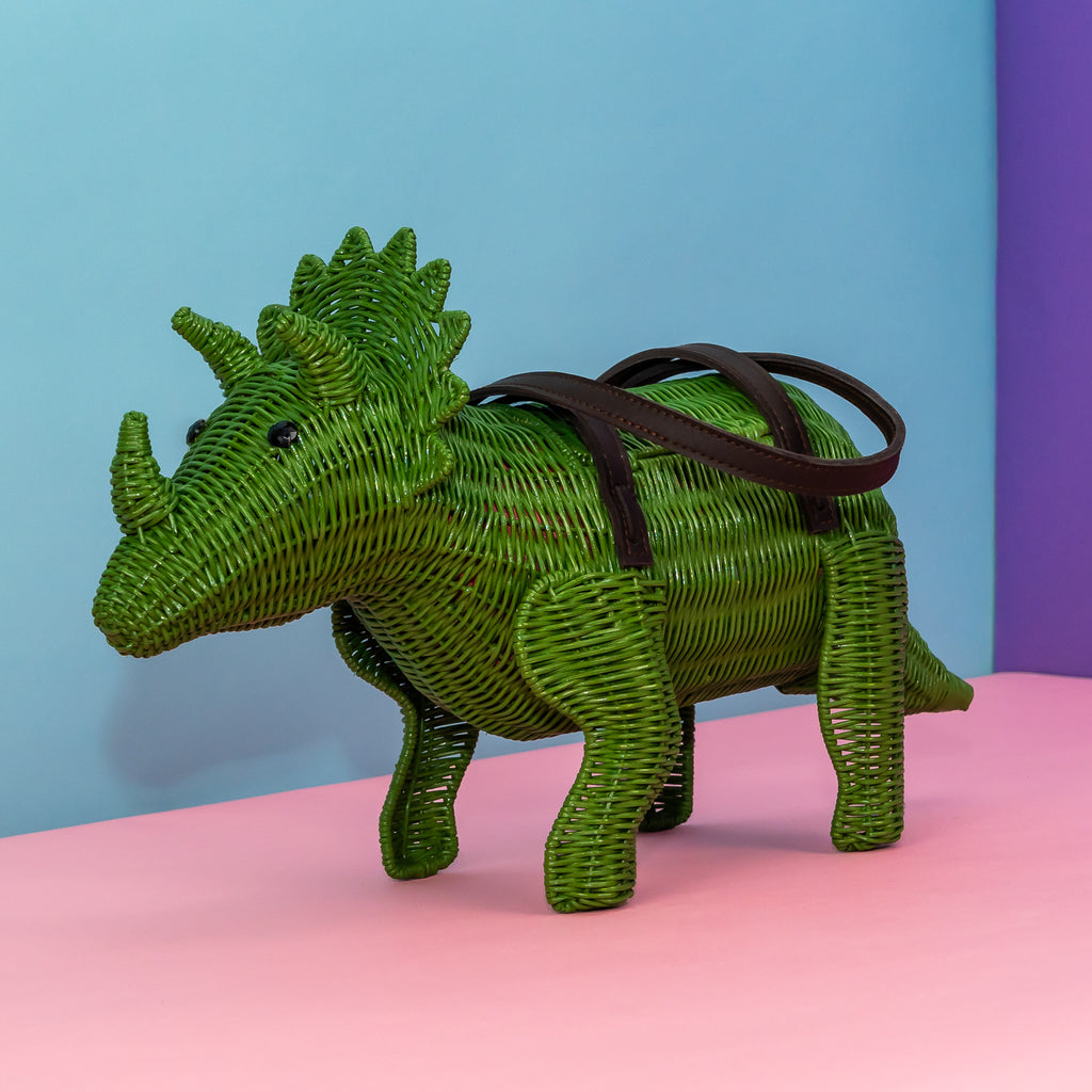 Wicker Darling green tirceratops purse dinosaur shaped bag sits in a colourful background.