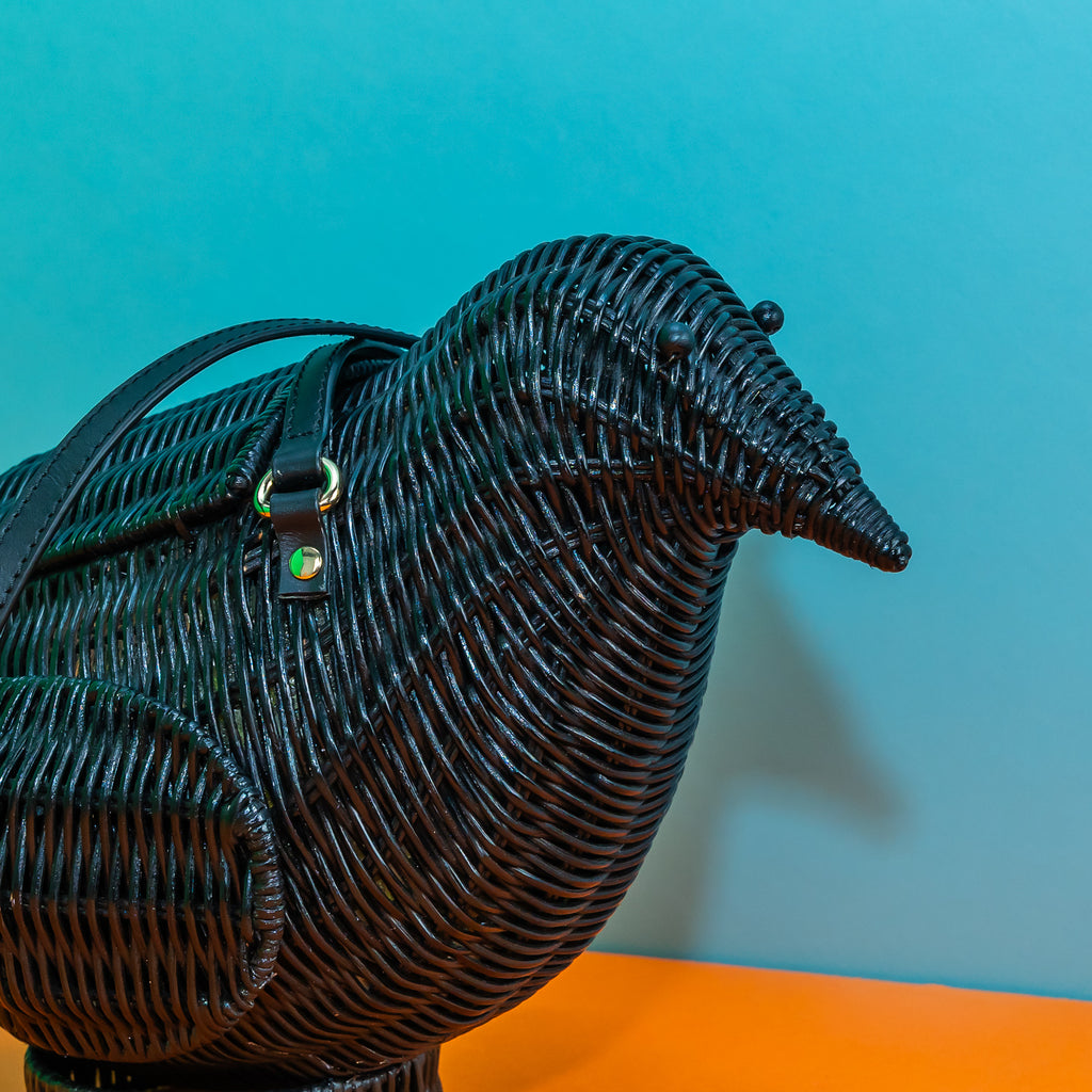 A close up on the face of a black rattan figural bag in the shape of a crow (or raven, or corvid, it is up to interpretation).