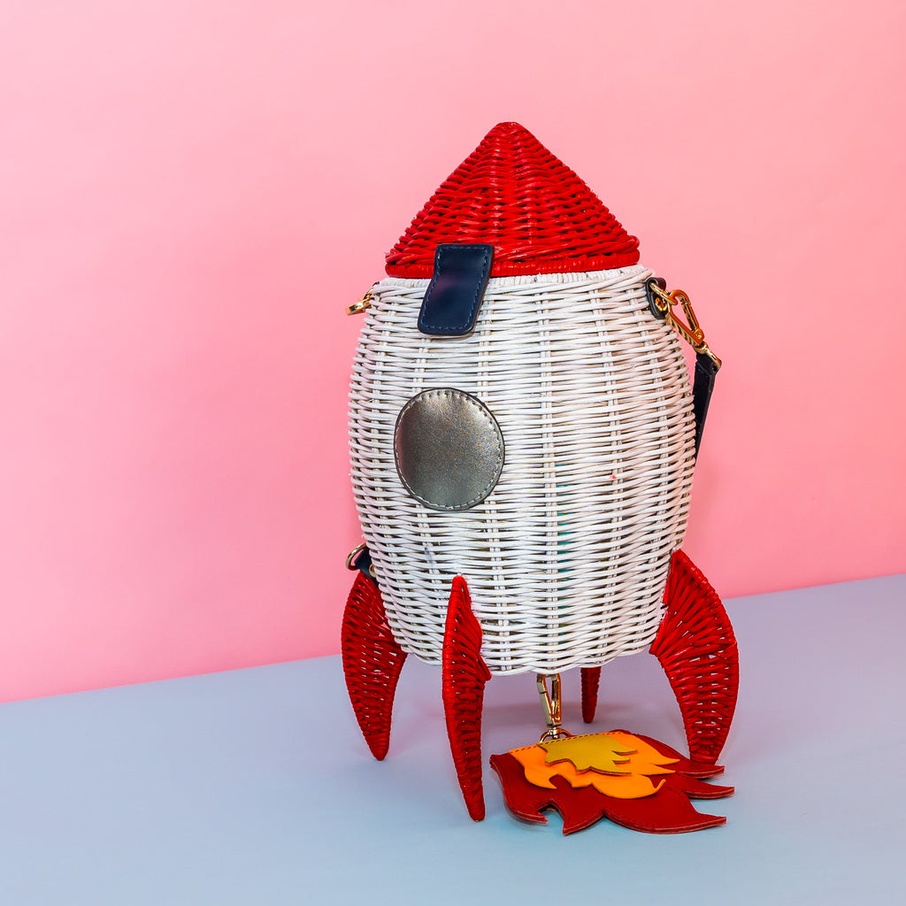 Wicker Darling handmade wicker rocket shaped purse rocket bag sits in a colourful background.