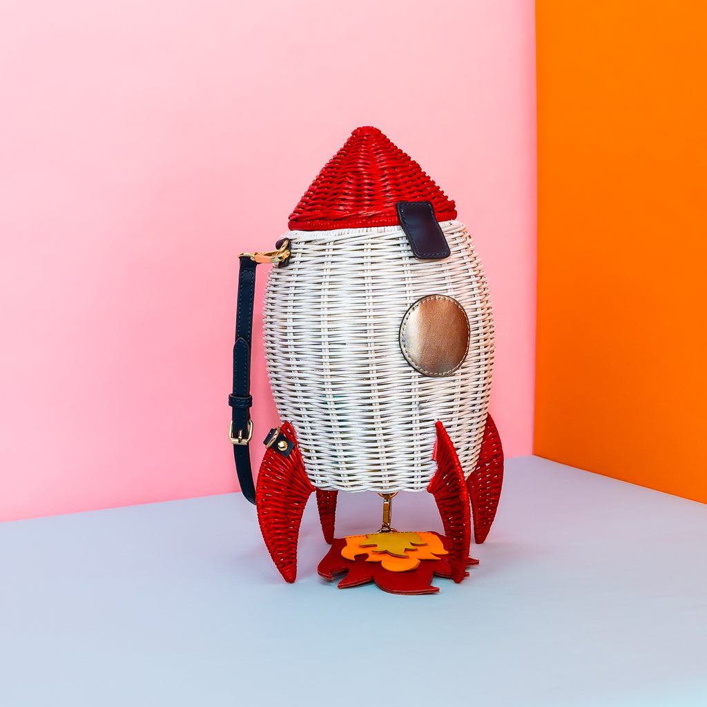 Wicker Darling handmade wicker rocket shaped purse rocket bag sits in a colourful background.