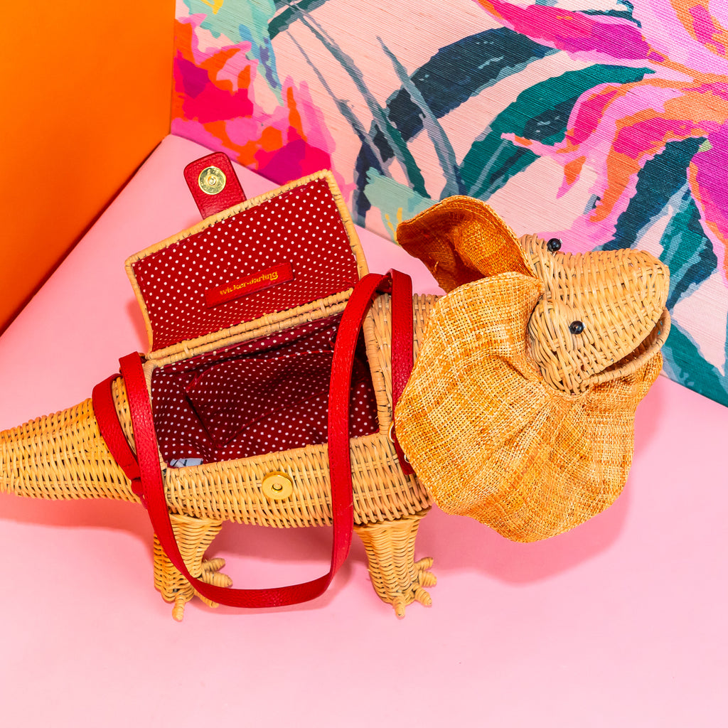 Wicker darling Priscilla Frillneck Wicker Lizard purse lizard handbag sits in a colourful background alongside colourful tropical wallpaper.