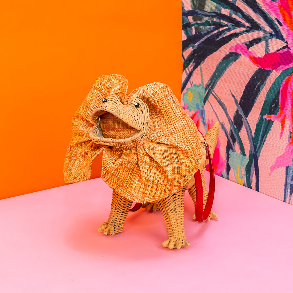 Wicker darling Priscilla Frillneck Wicker Lizard purse lizard handbag sits in a colourful background alongside colourful tropical wallpaper.