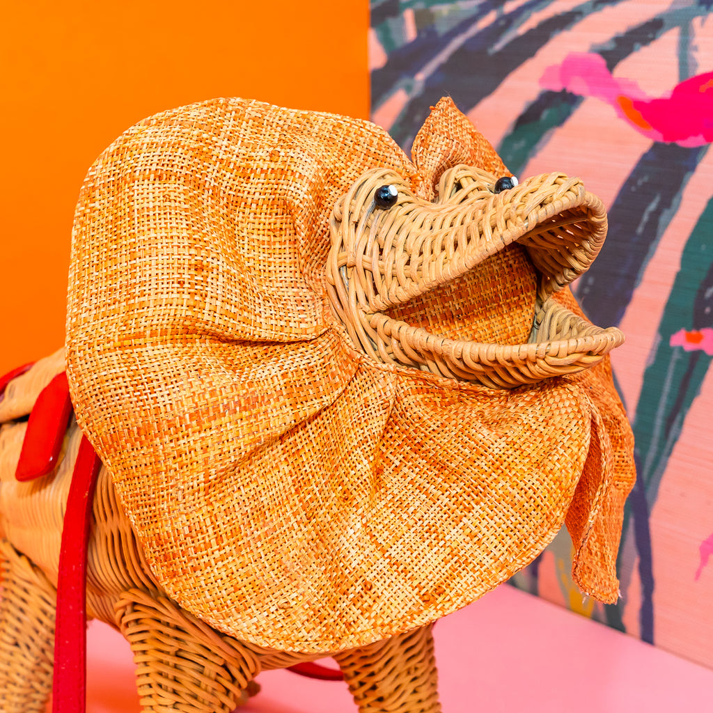 Wicker darling Priscilla Frillneck Wicker Lizard purse lizard handbag sits in a colourful background alongside colourful tropical wallpaper.