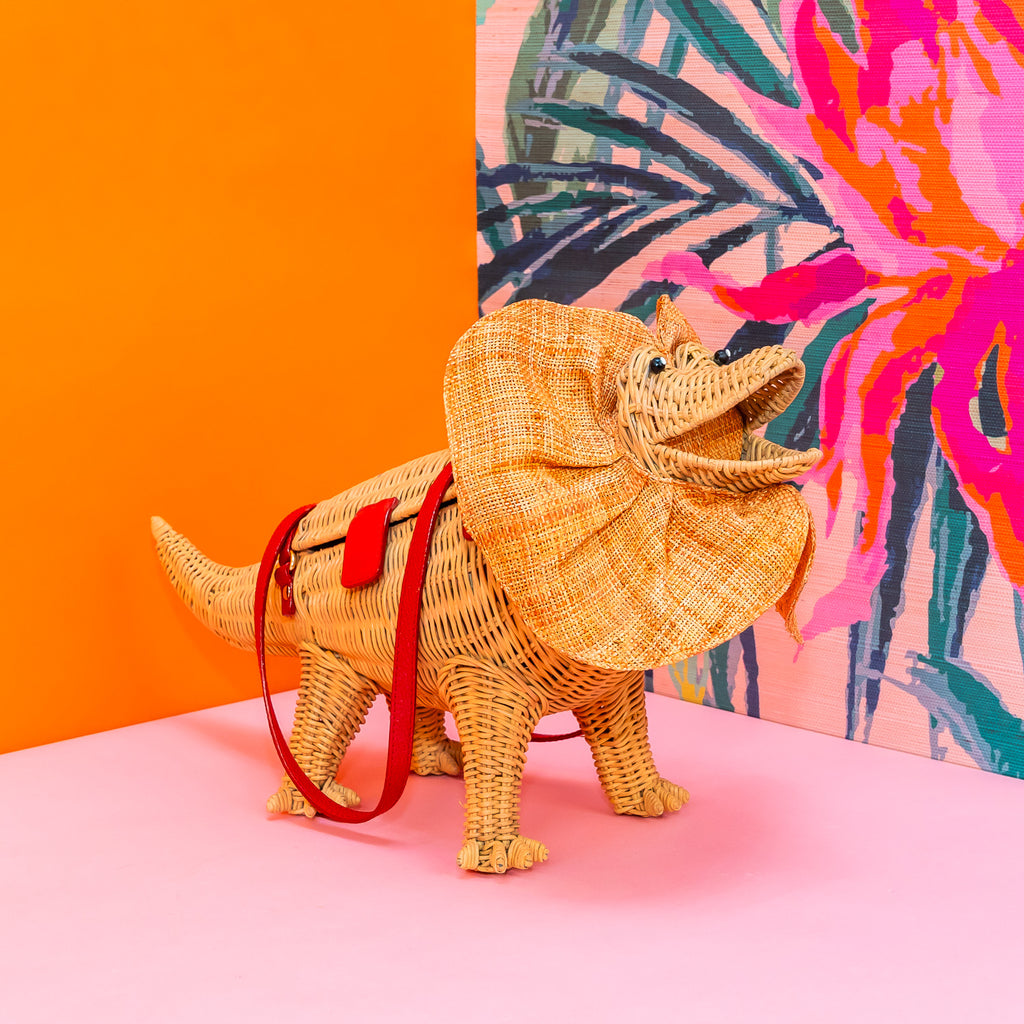 Wicker darling Priscilla Frillneck Wicker Lizard purse lizard handbag sits in a colourful background alongside colourful tropical wallpaper.