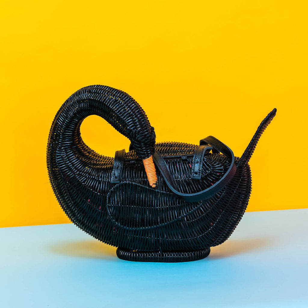 Wicker darling odile black swan purse black swan handbag sits in a colourful yellow and blue background. 