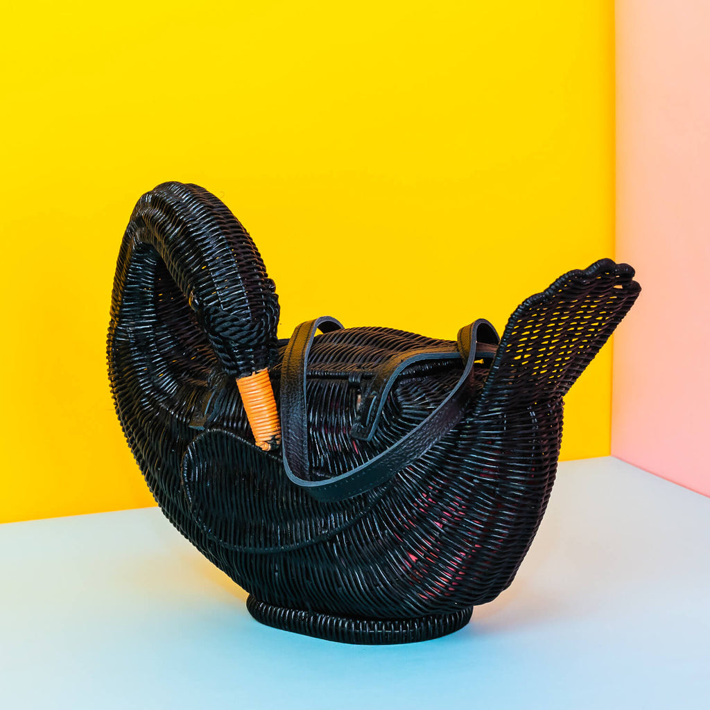 Wicker darling odile black swan purse black swan handbag sits in a colourful yellow and blue background. 