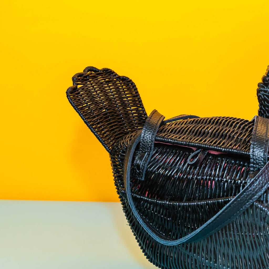 Wicker darling odile black swan purse black swan handbag sits in a colourful yellow and blue background. 