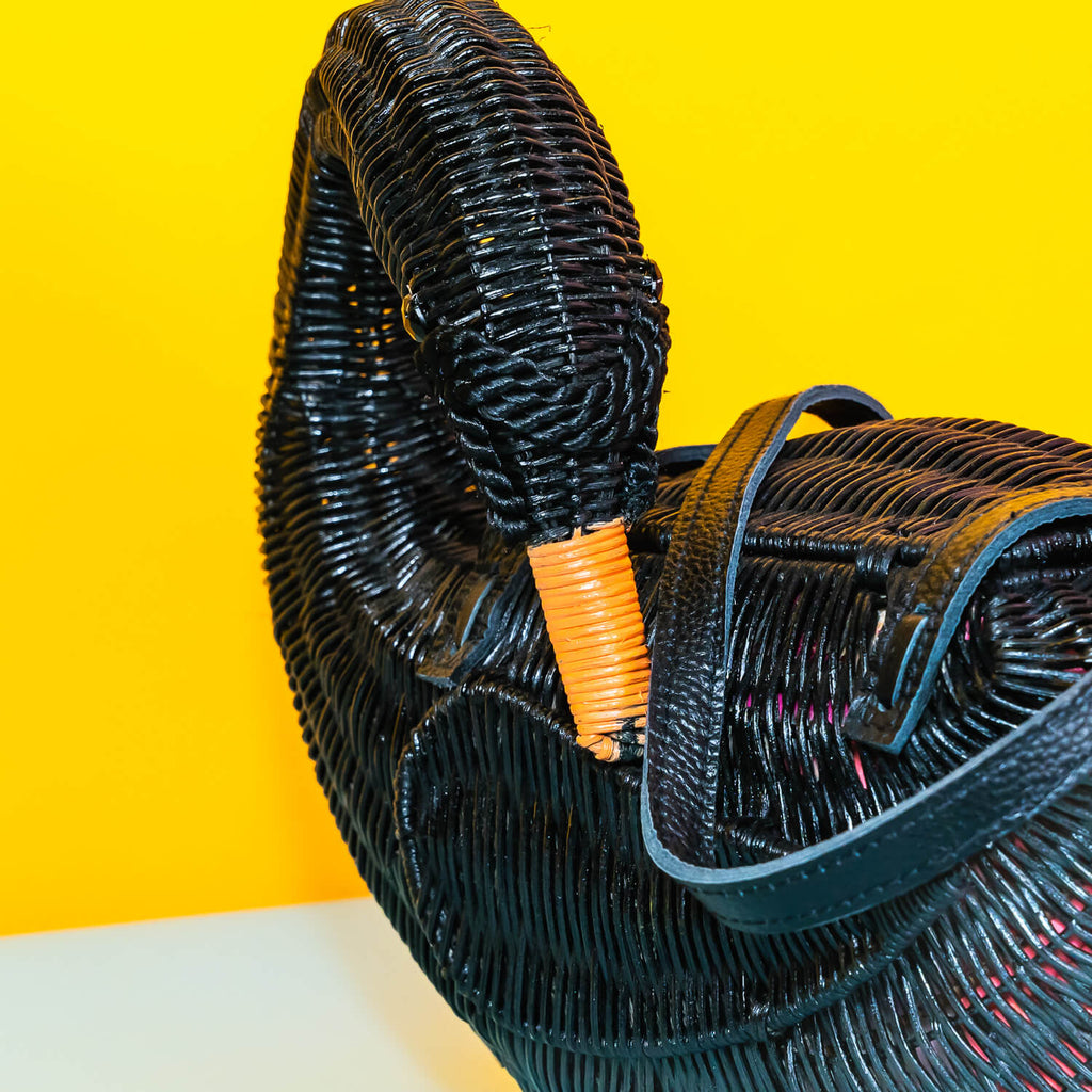 Wicker darling odile black swan purse black swan handbag sits in a colourful yellow and blue background. 