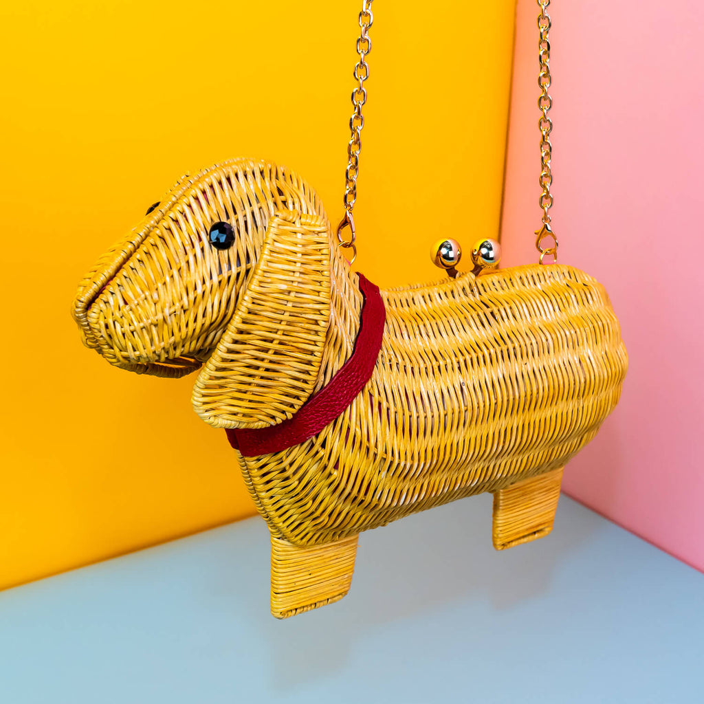 Wicker Darling yellow sausage dog clutch purse sausage dog handbag hands in a colourful room.