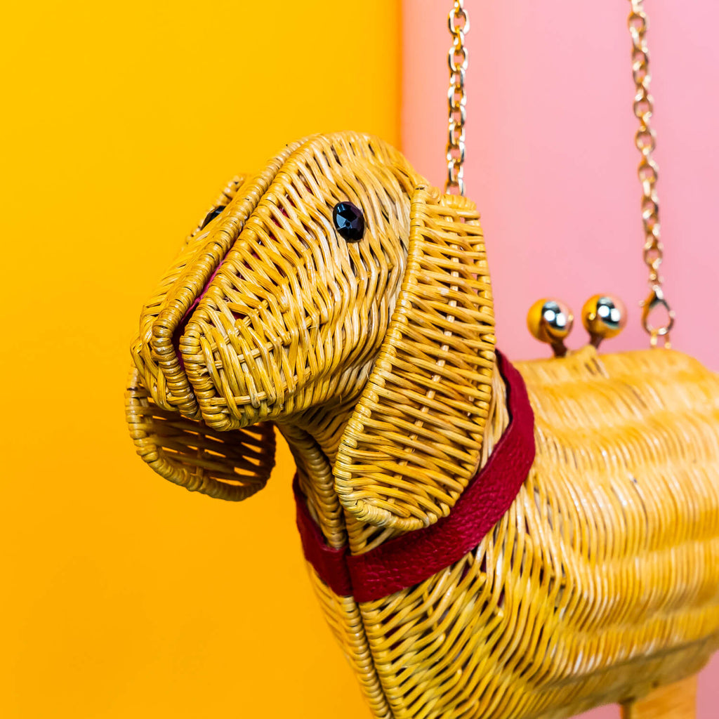 Wicker Darling yellow sausage dog clutch purse sausage dog handbag hands in a colourful room.