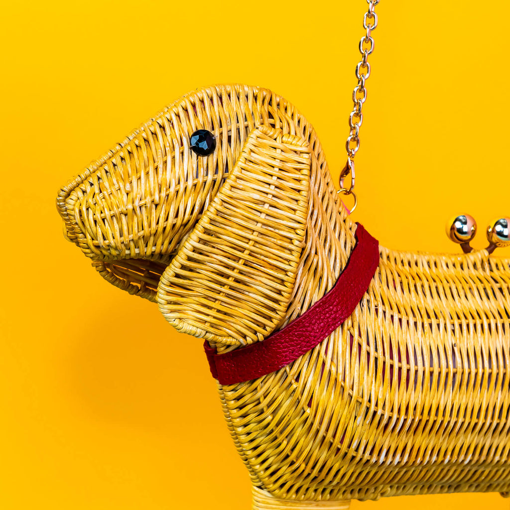 Wicker Darling yellow sausage dog clutch purse sausage dog handbag hands in a colourful room.