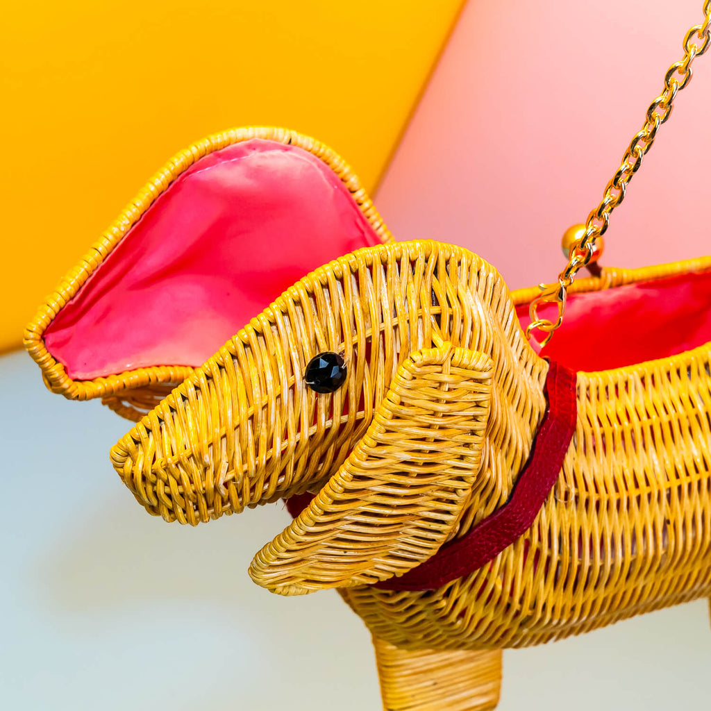 Wicker Darling yellow sausage dog clutch purse sausage dog handbag hands in a colourful room.