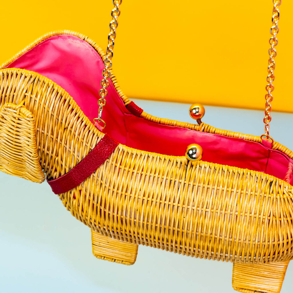 Wicker Darling yellow sausage dog clutch purse sausage dog handbag hands in a colourful room.