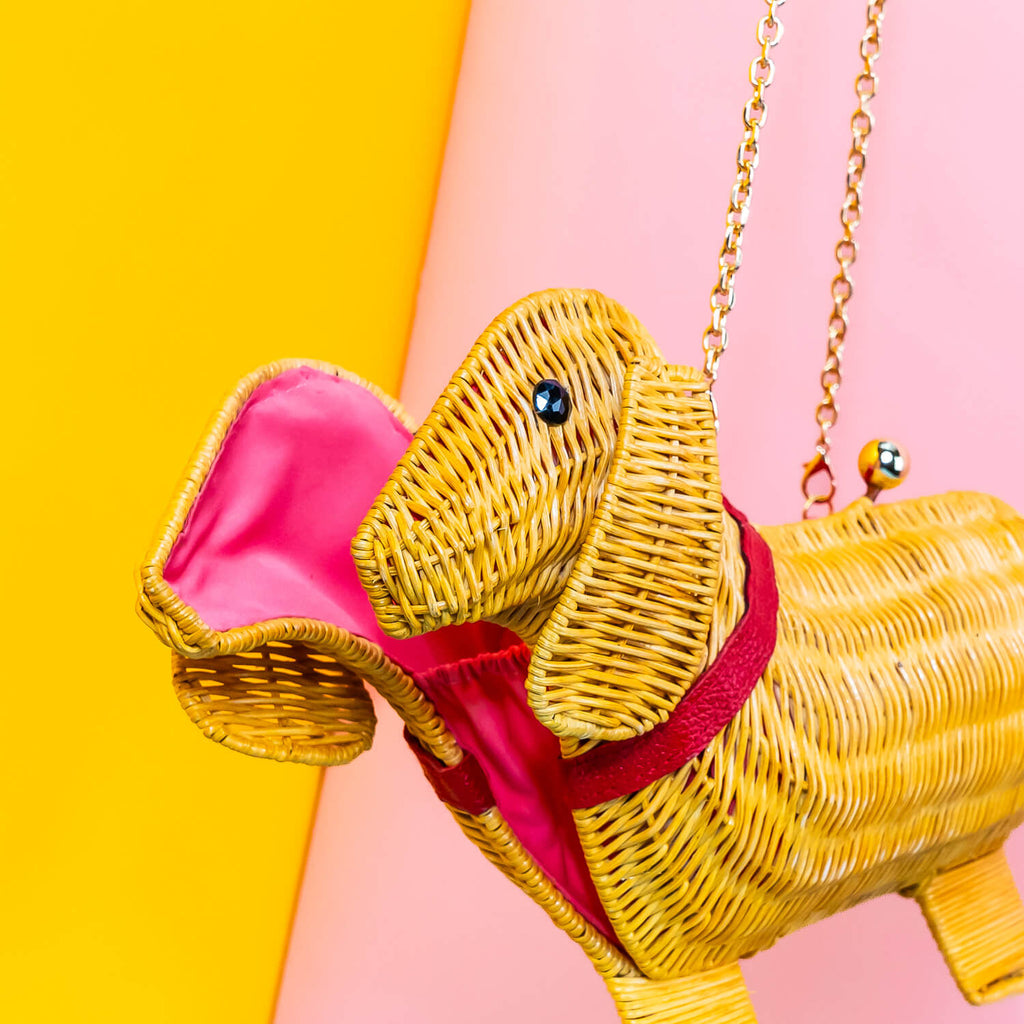 Wicker Darling yellow sausage dog clutch purse sausage dog handbag hands in a colourful room.