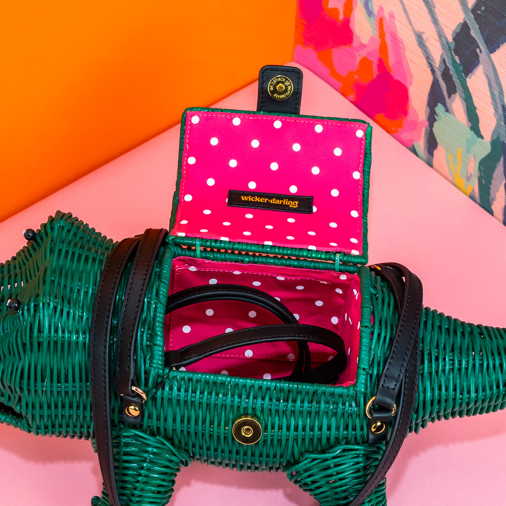 A view inside Wicker Darling's crocodile novelty purse. The bag has pink lining with white polka dots, and a magnetic closure. The black leather straps are attached on gold-coloured metal D-rings, which allows a detachable black leather crossbody strap to be attached to the bag.