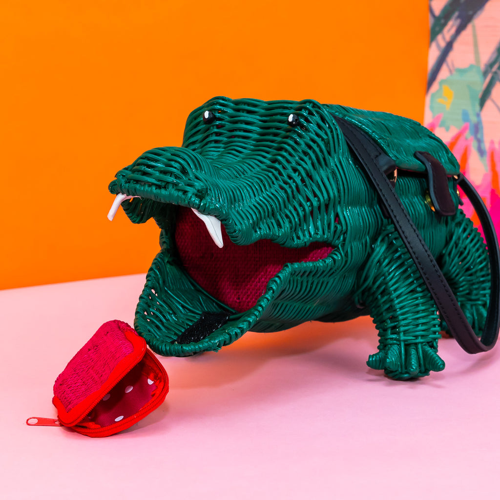 A close up of a crocodile shaped wicker handbag, featuring the mouth of the crocodile. It has white leather teeth, and the reddish pink tongue sits in front, revealing that it's actually a coin purse with zip closure and pink and white polka dot lining.