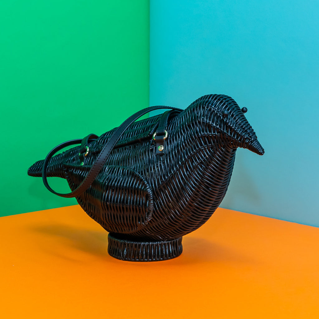 A rattan bag in the shape of a bird. It is painted black, implying the bag is a corvid (crow, raven, or jackdaw) bag.