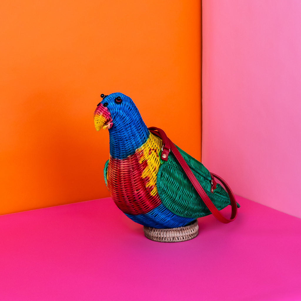 Wicker darling rainbow lorikeet parrot handbag wicker parrot purse sits in a colourful background.