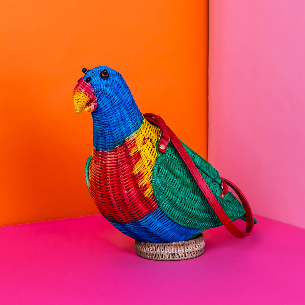 Wicker darling rainbow lorikeet parrot handbag wicker parrot purse sits in a colourful background.