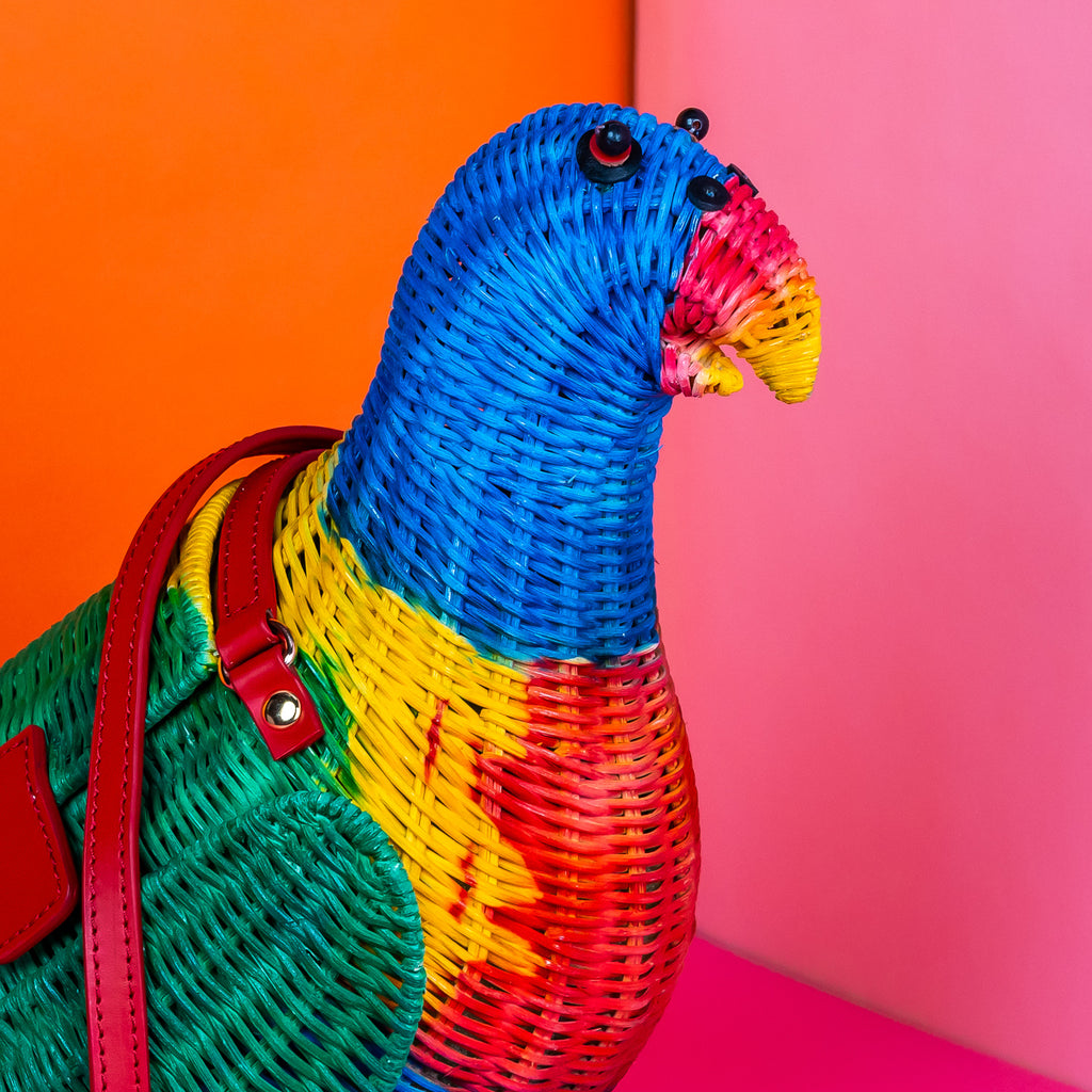 Wicker darling rainbow lorikeet parrot handbag wicker parrot purse sits in a colourful background.