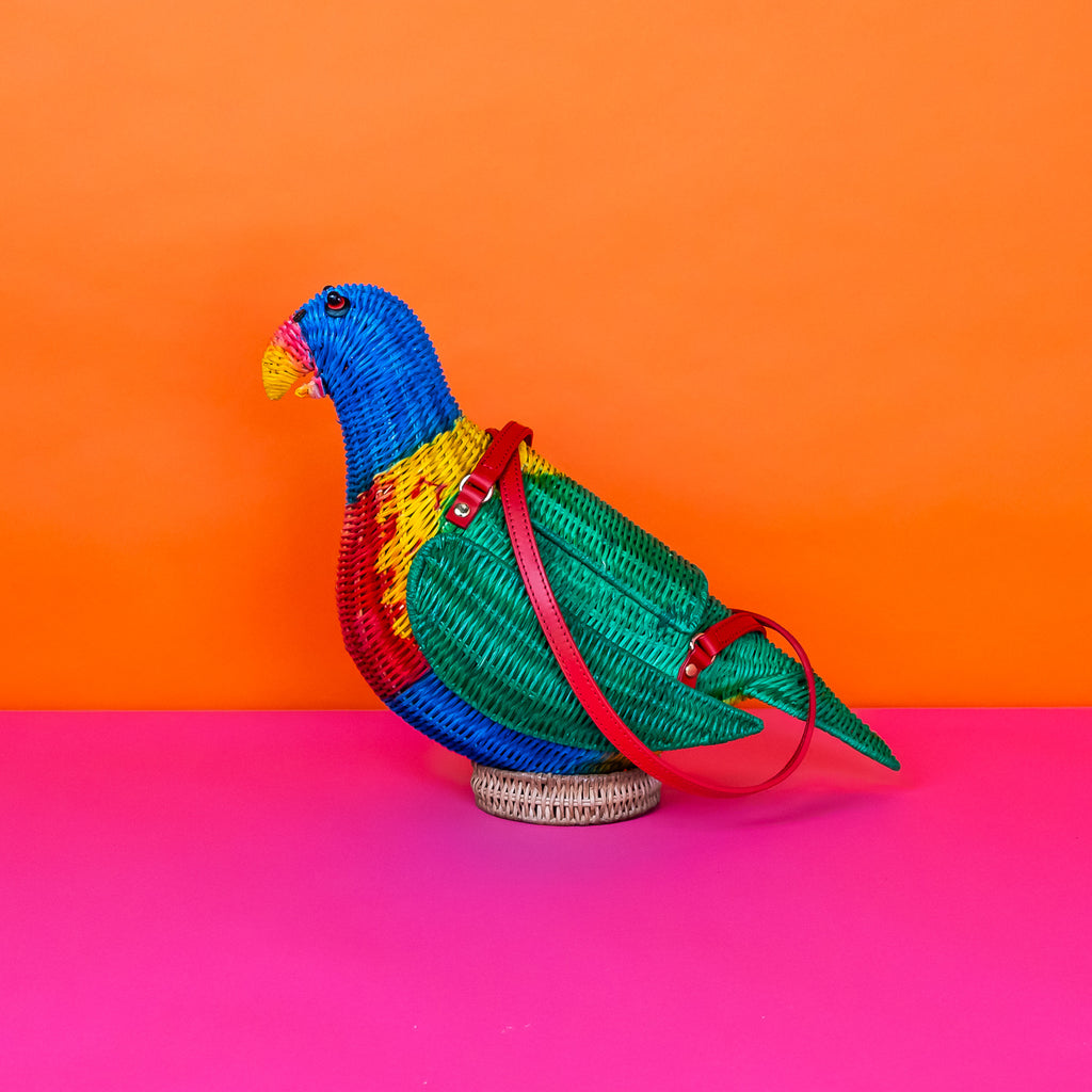 Wicker darling rainbow lorikeet parrot handbag wicker parrot purse sits in a colourful background.