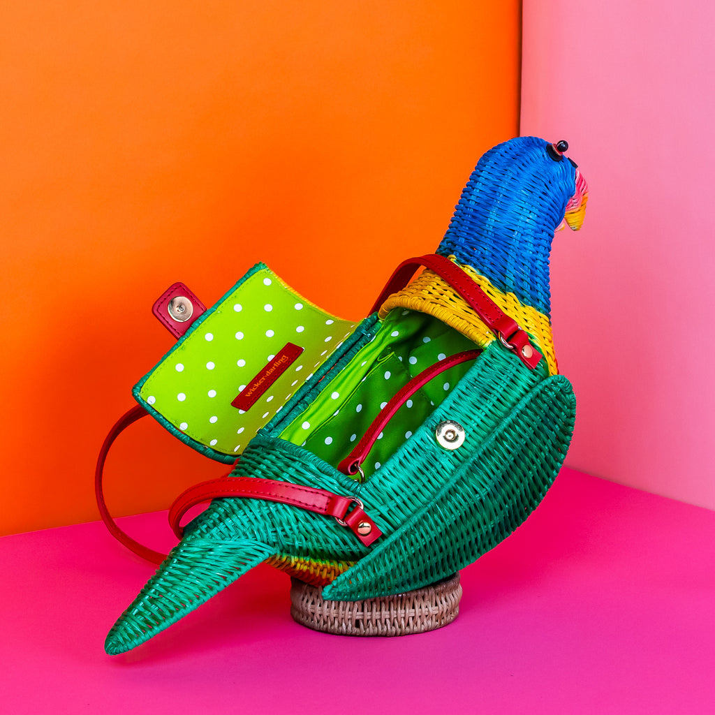 Wicker darling rainbow lorikeet parrot handbag wicker parrot purse sits in a colourful background.