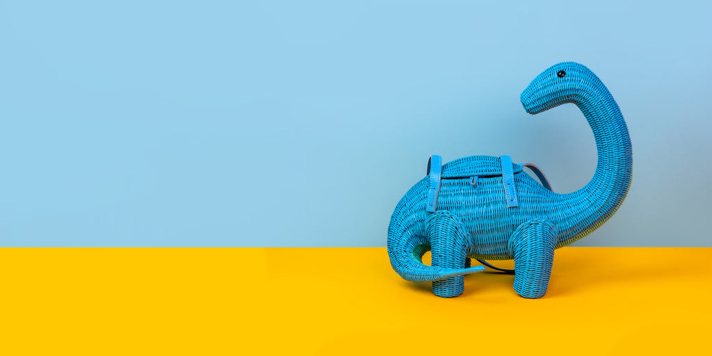 Wicker Darling blue brontesaurus purse dinosaur shaped bag sits in a colourful background