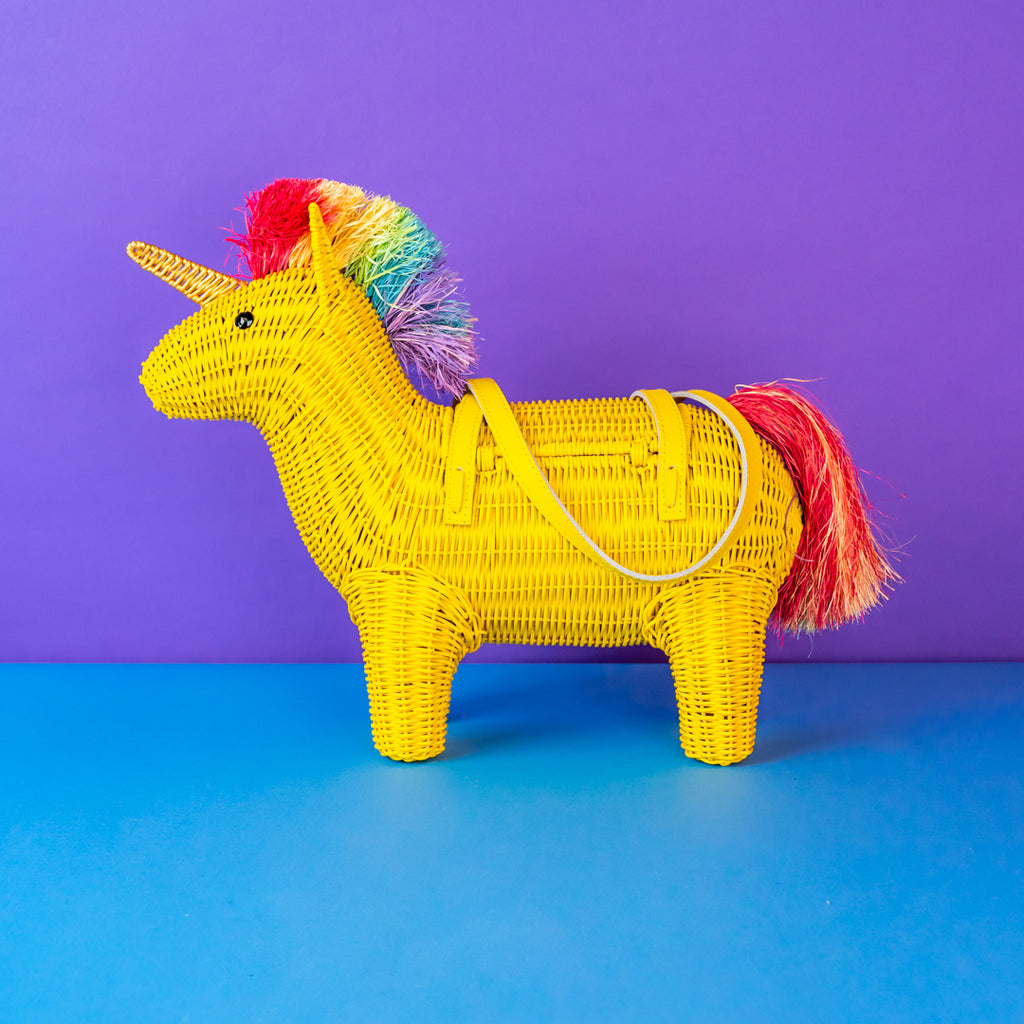 Yellow woven unicorn handbag with a rainbow mane on a blue surface with a purple background