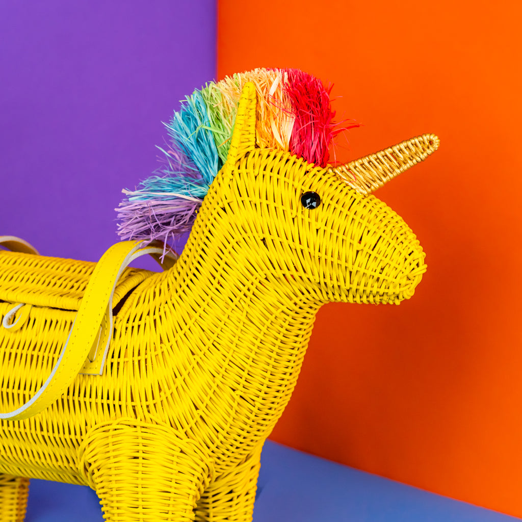 Yellow woven unicorn handbag with rainbow hair against a colorful background