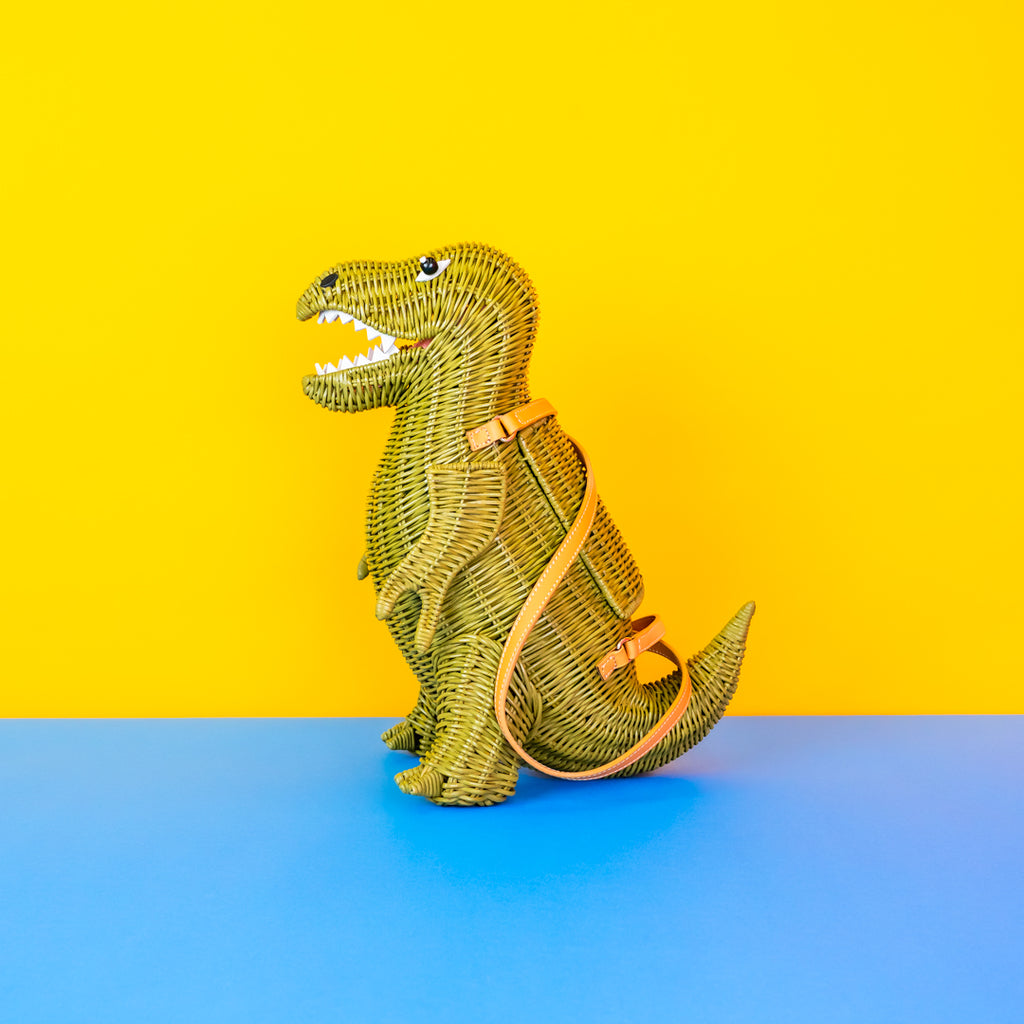 Wicker dinosaur bag with tan leather straps on a yellow and blue background