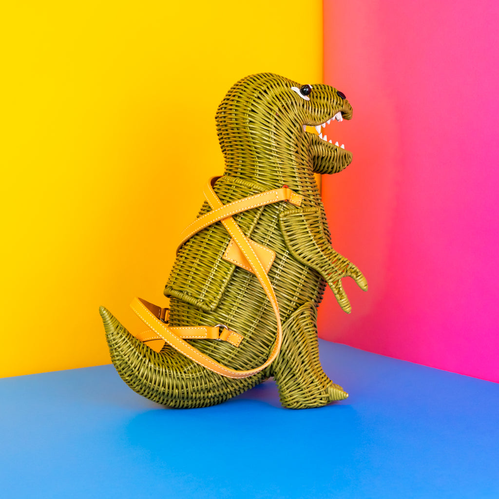 Wicker t-rex dinosaur handbag with long pointed tail. The dinosaur is painted green and has tan handles.