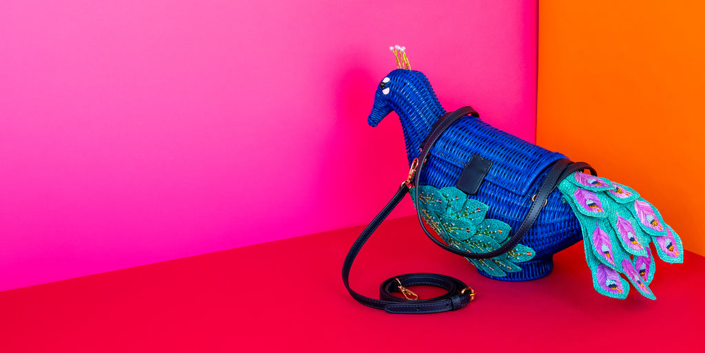 Wicker Darling Purseus the Peacock purse peacock shaped handbag is deep blue and features ornate embroidery and beading on it's tail and sits in a colourful room.