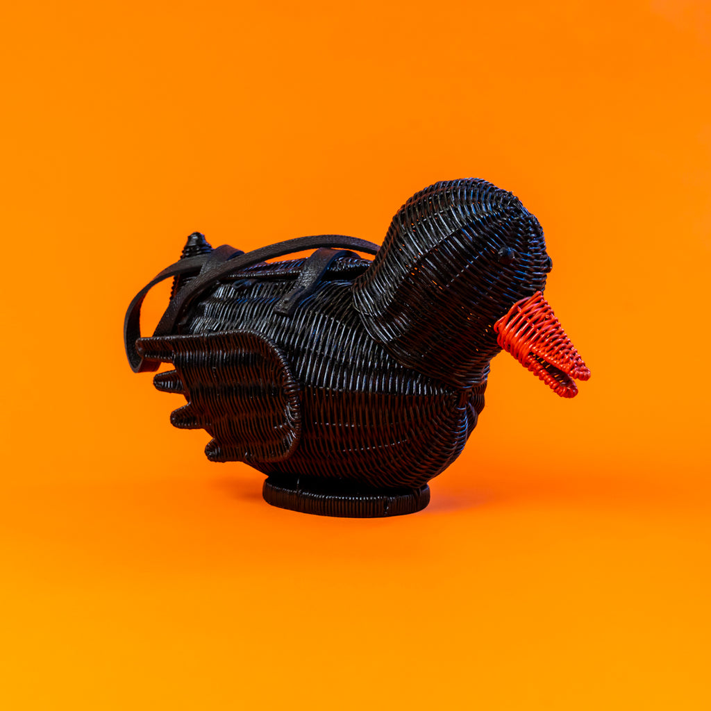 Black rubber ducky bag made from rattan on an orange backdrop.

