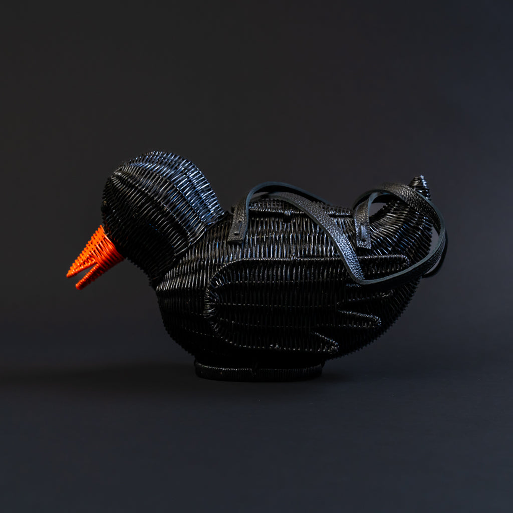 Black woven bird sculpture with an orange beak on a dark background