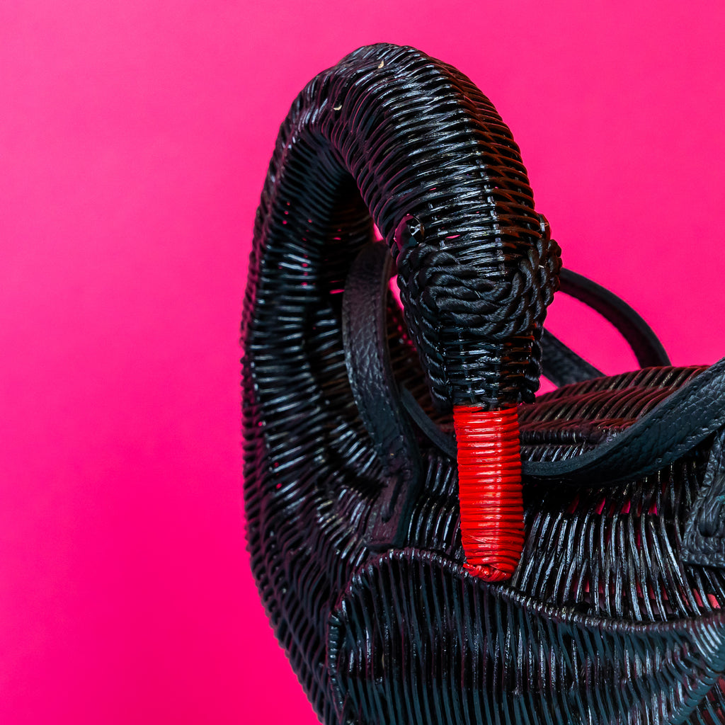 Wicker darling Odile the black swan purse swan handbag sits in a colourful background.