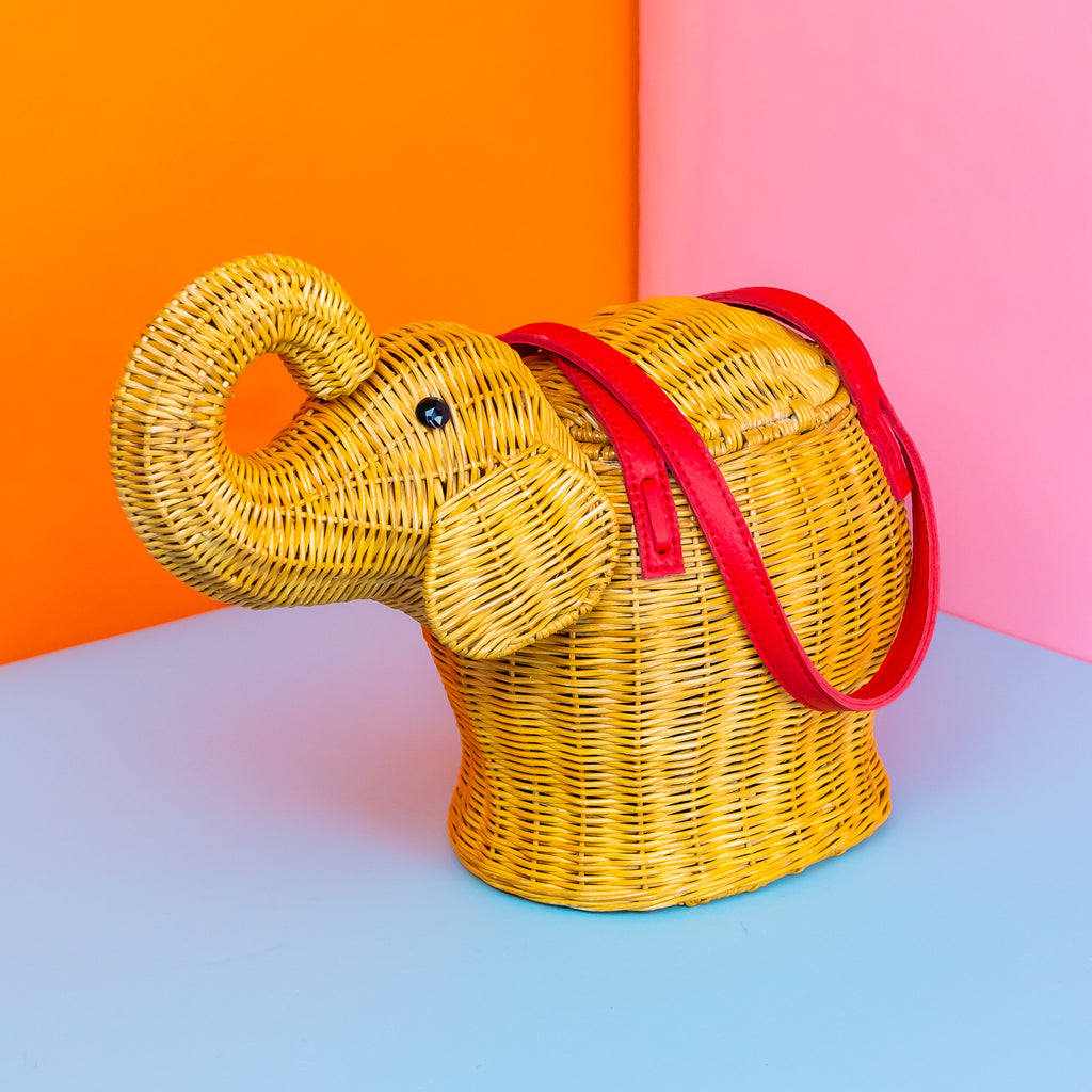 A trunk-up elephant shaped wicker bag with red leather handles.