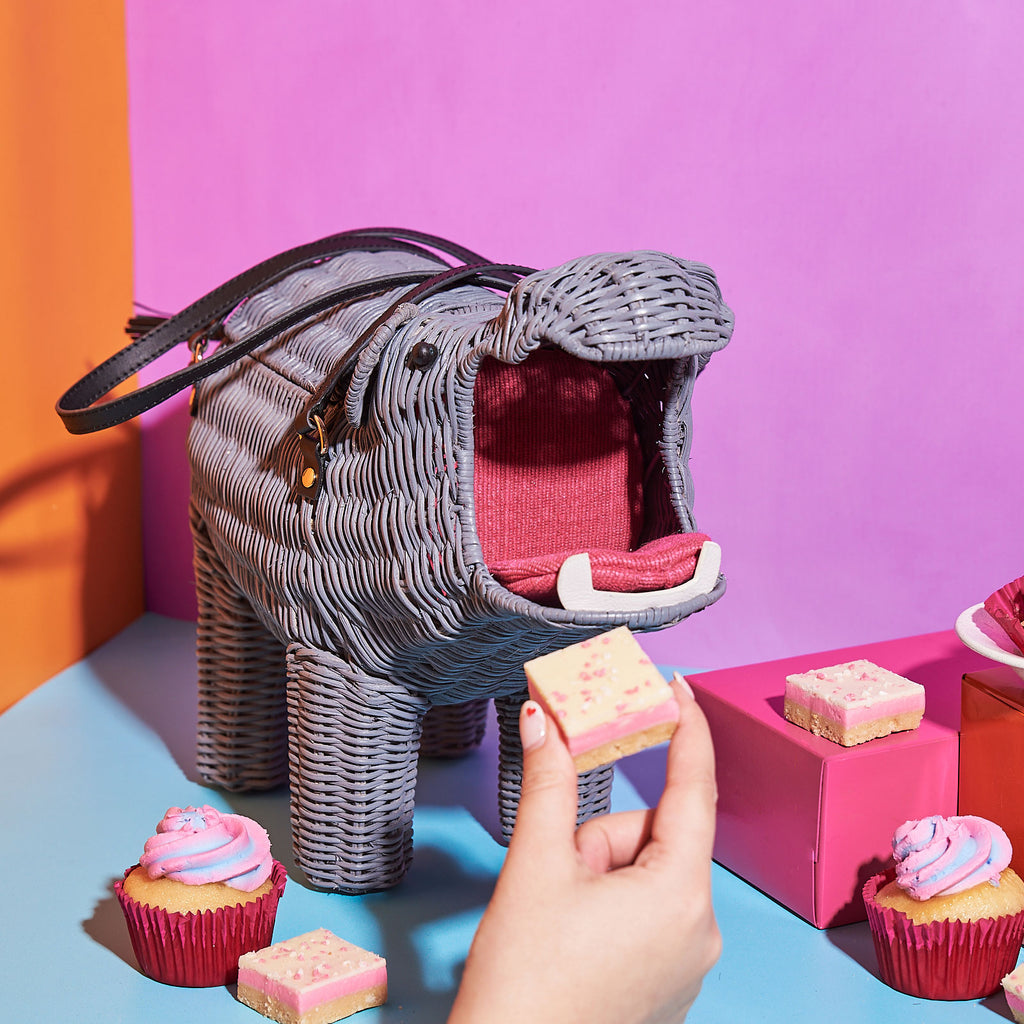 Animal Handbags Wicker Darling Hippolyta the hippo shaped purse sits eating sweets in a colourful background